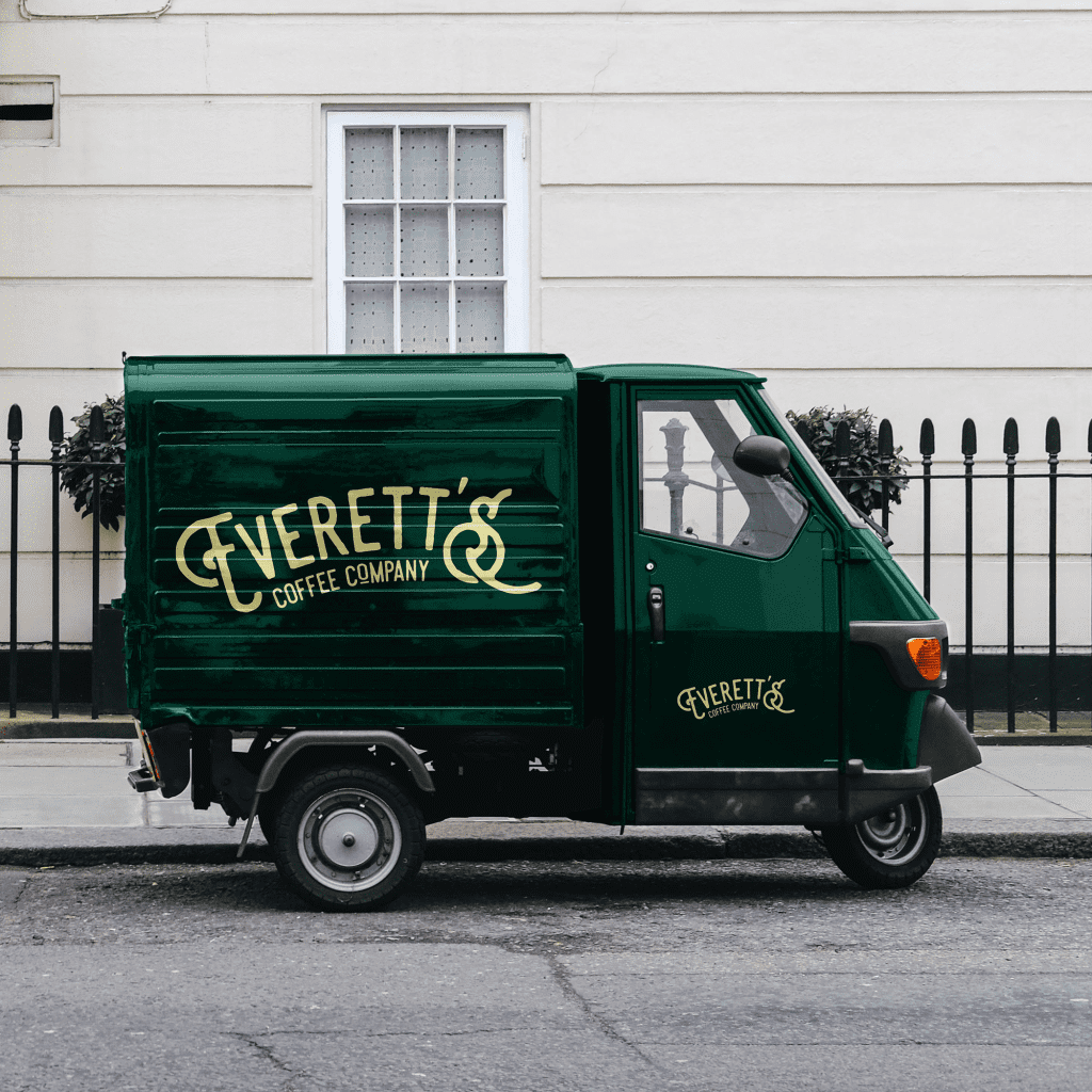 Vintage green van with Everetts coffee company logo on the side in gold, parked outside an elegant building.