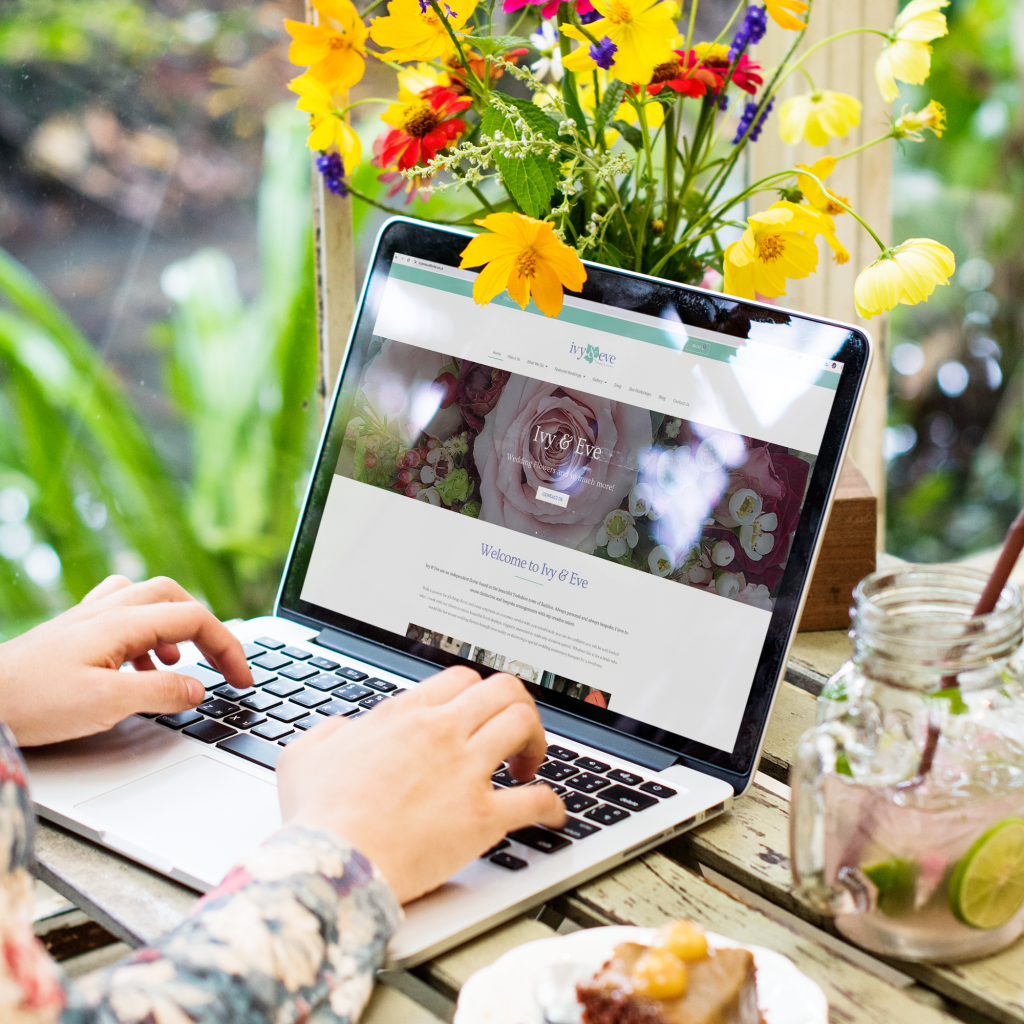 Lady viewing a floristry website on her laptop whilst surrounded by beautiful flowers